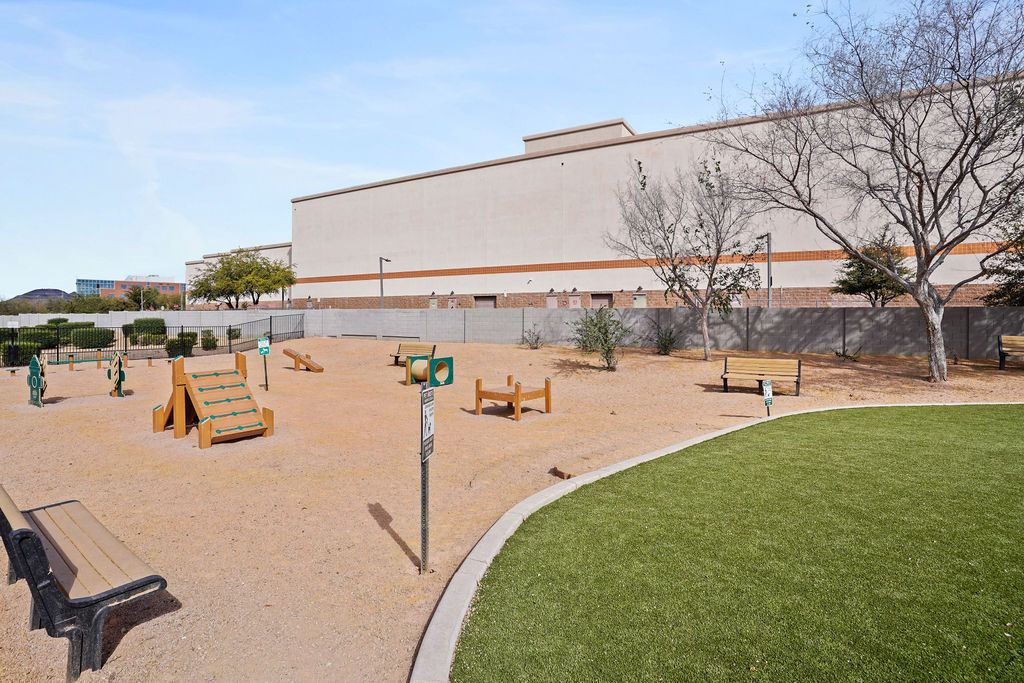 Outdoor playground with wooden play structures, benches, and a curved grass edge beside a large building at Heritage at Deer Valley in Phoenix, AZ.