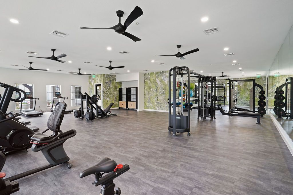 Interior of a modern fitness center with cardio machines, free weights, mirrors, and ceiling fans at Heritage at Deer Valley in Phoenix, AZ.
