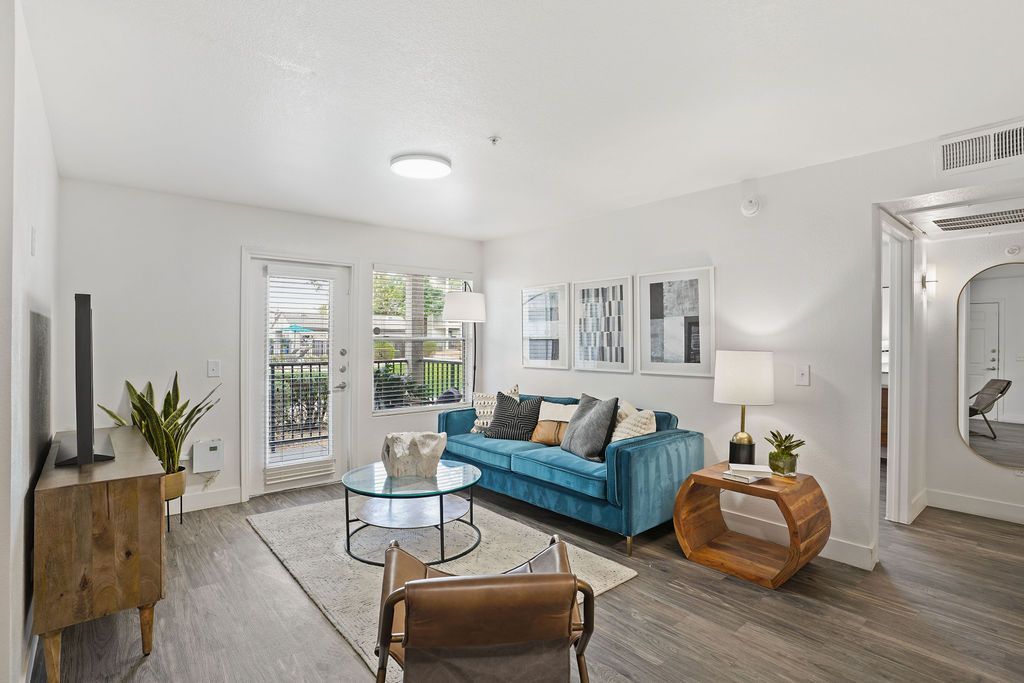 Living room with teal sofa, round glass coffee table, TV, and balcony door in a modern apartment at Heritage at Deer Valley in Phoenix, AZ.