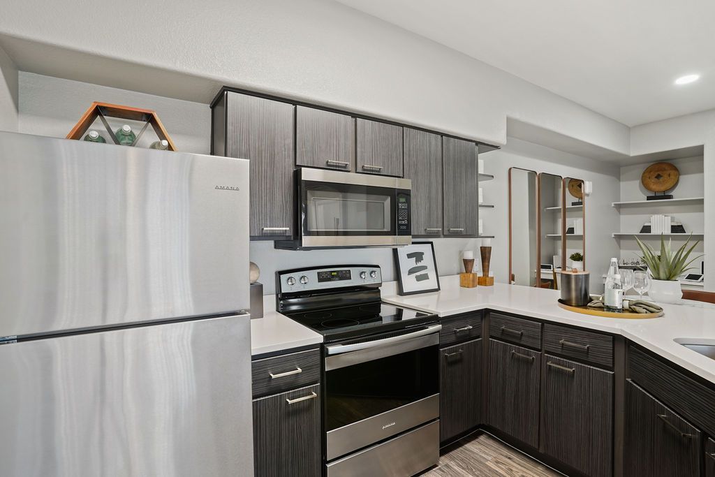 Modern apartment kitchen with stainless steel refrigerator, microwave, stove, and dark wood cabinets at Heritage at Deer Valley in Phoenix, AZ.