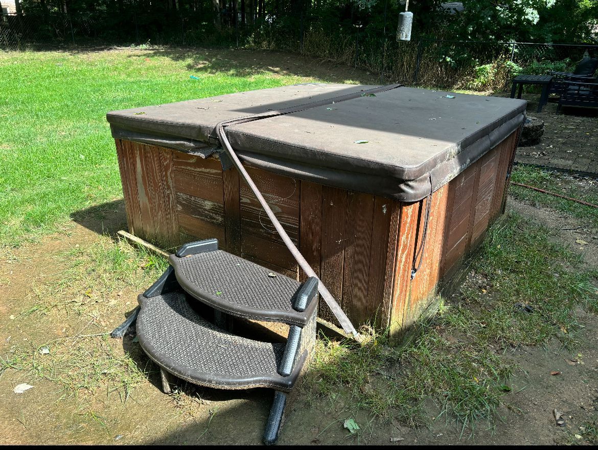 Brown wooden hot tub with closed cover and steps on green grass.
