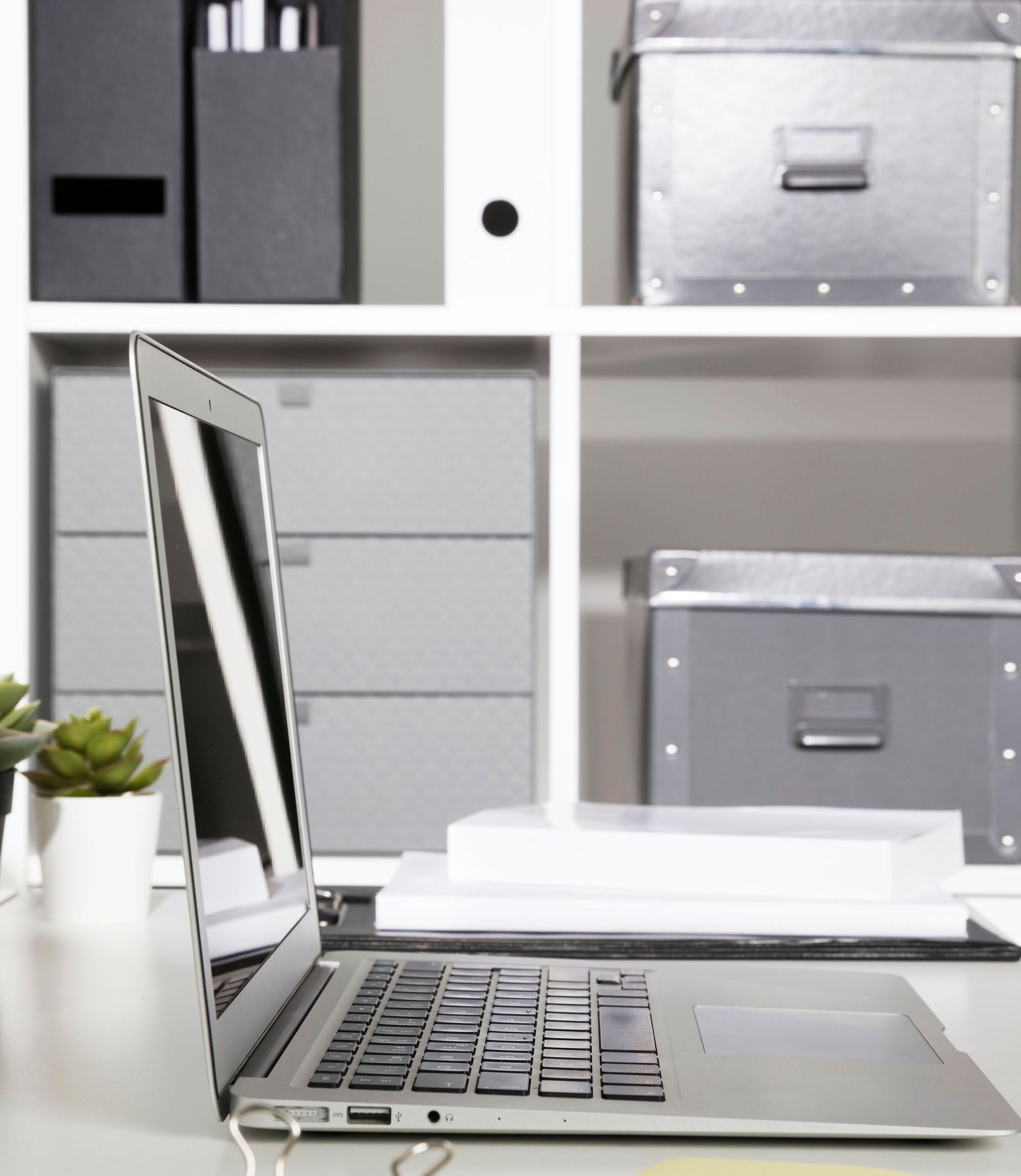 A laptop is open on a desk in front of a shelf