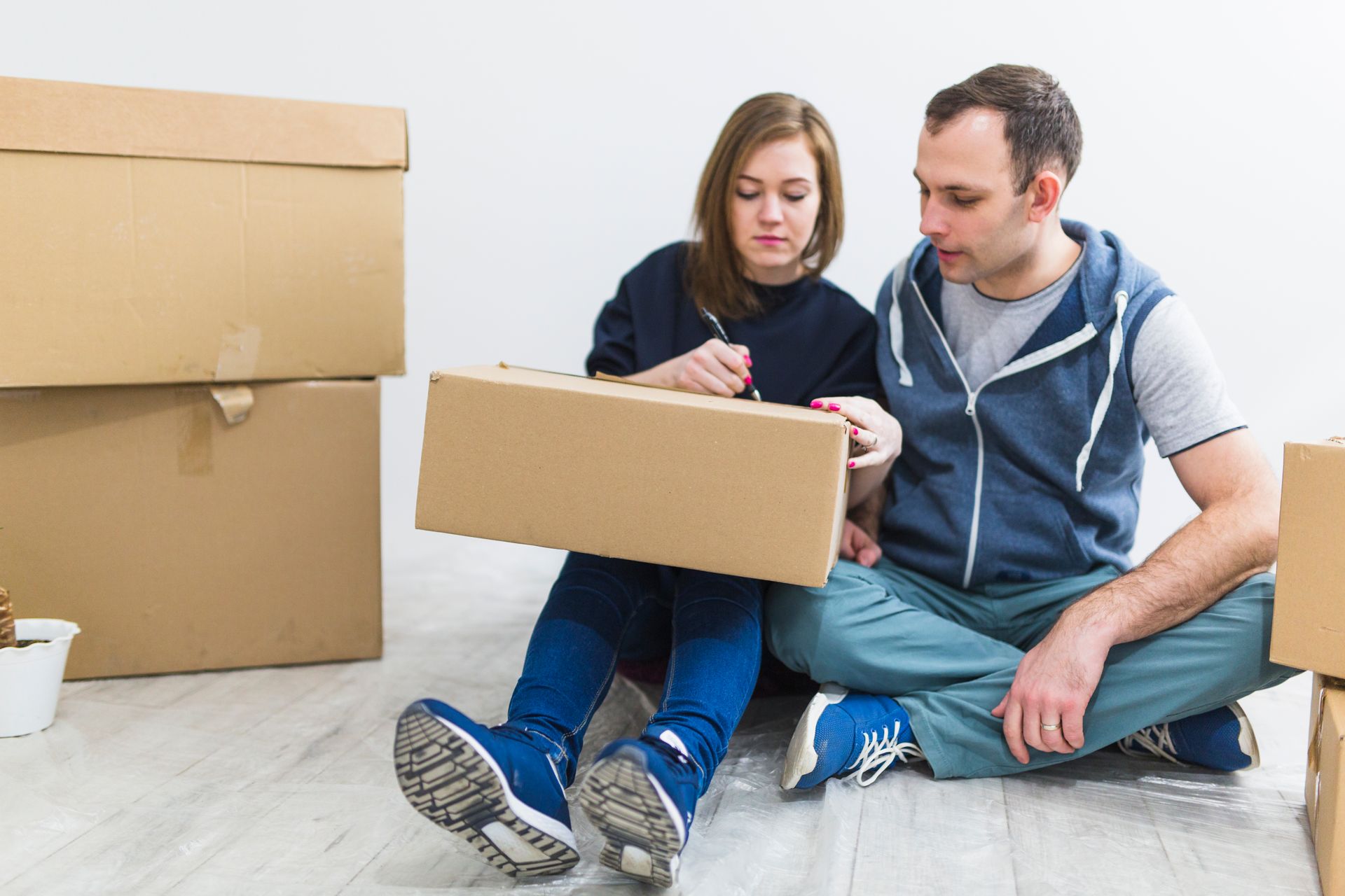 A man and a woman are sitting on the floor with cardboard boxes.