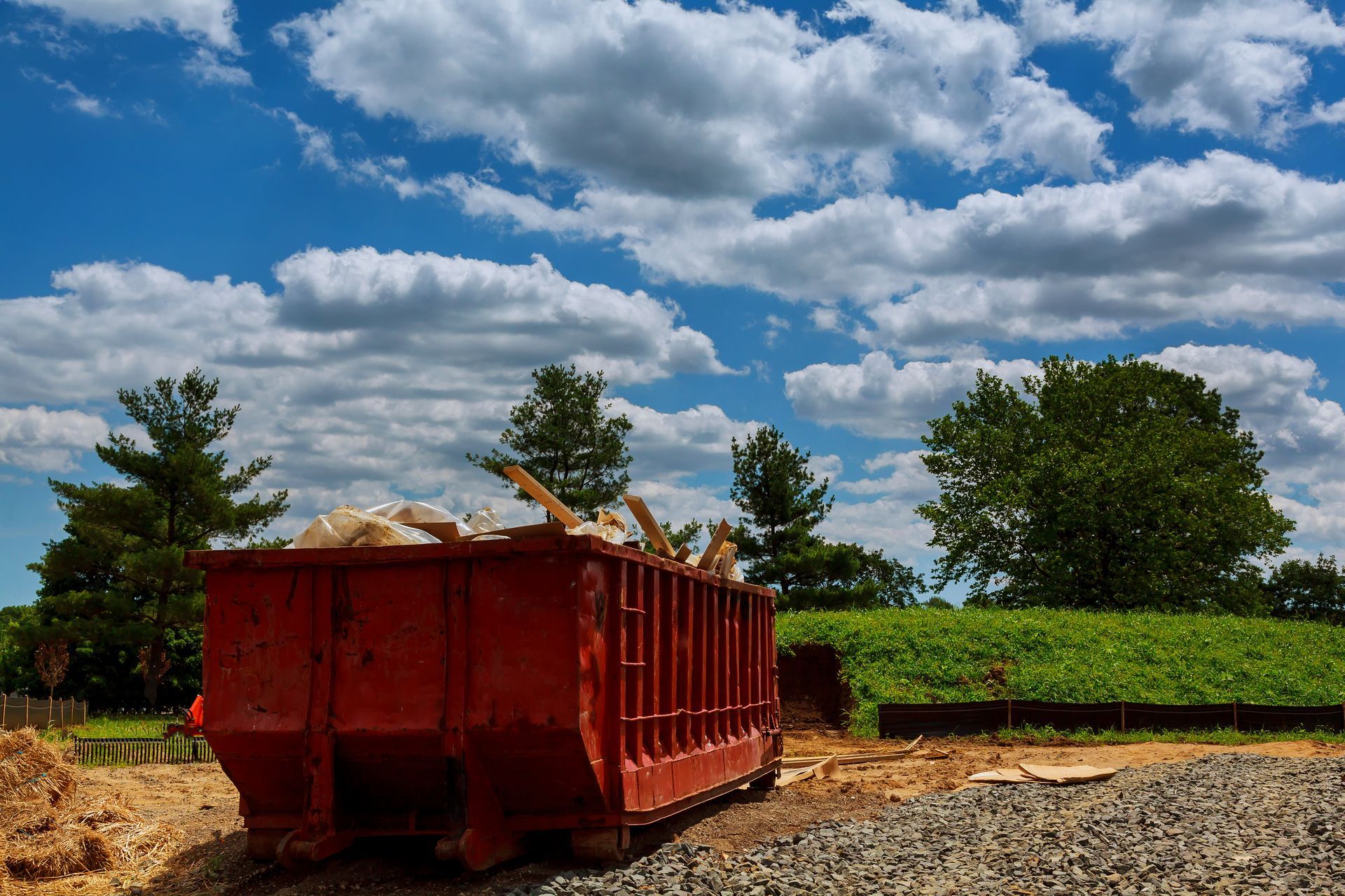 A large red dumpster is sitting on top of a dirt field.