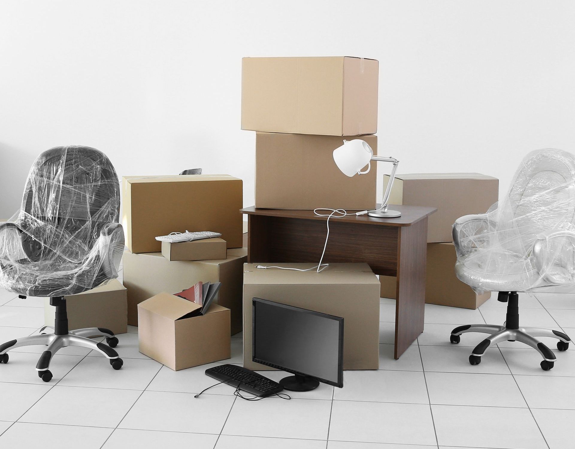 A room filled with boxes , chairs , a desk and a computer monitor.