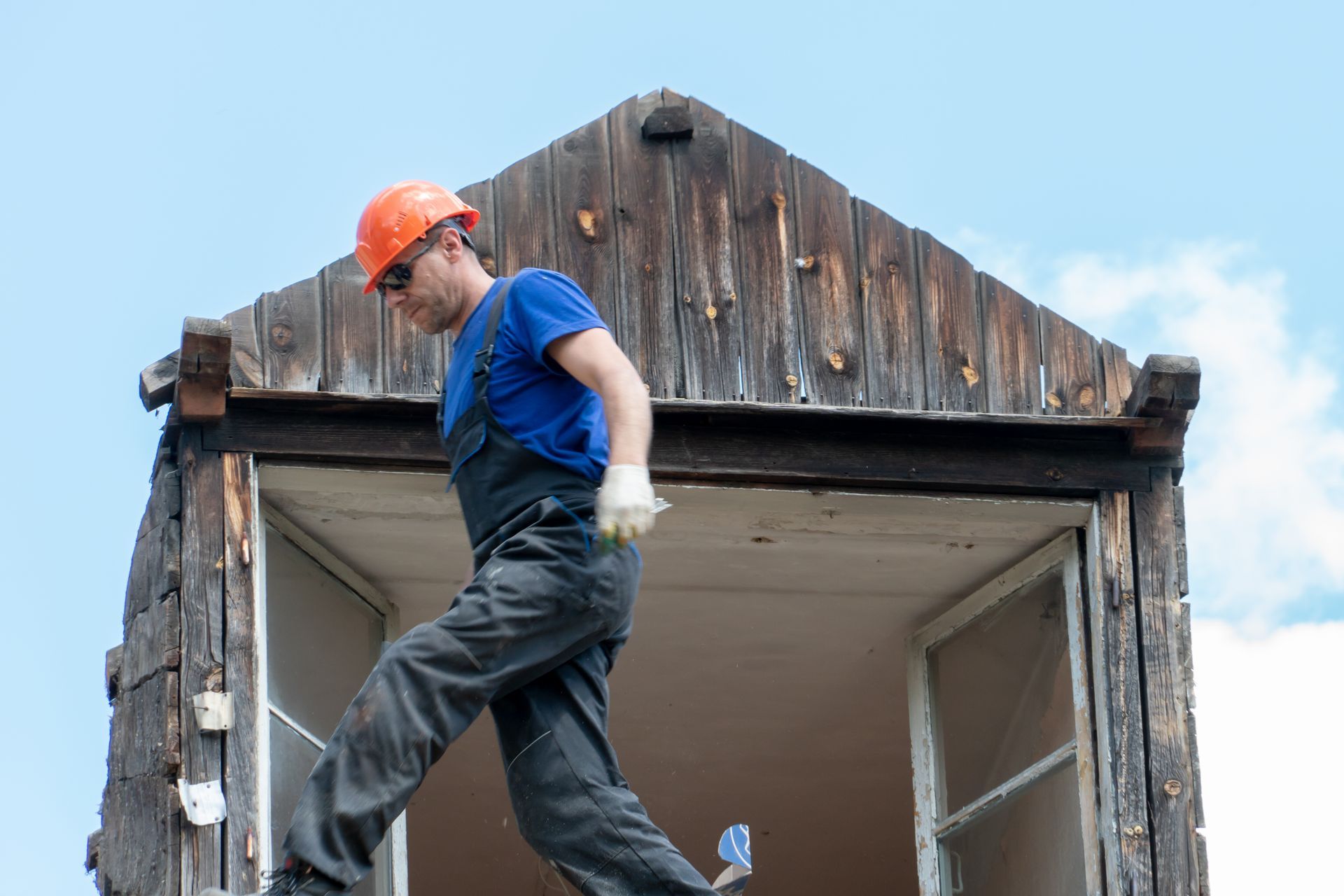 A man wearing a hard hat is standing on top of a wooden building.