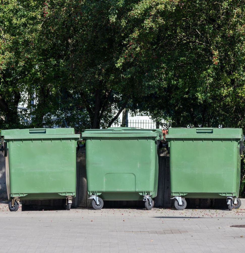 Three green dumpsters are parked in a parking lot