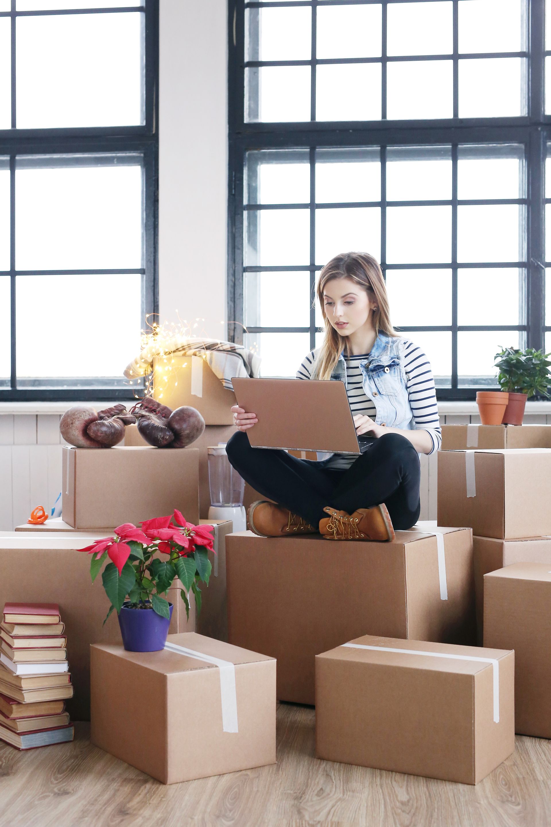 A woman is sitting on a pile of cardboard boxes using a laptop computer.