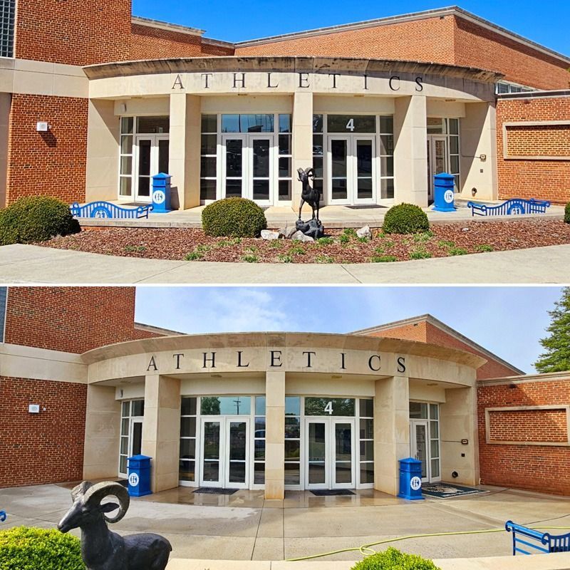 School athletics entrance with brick facade, white columns, blue trash bins, and a ram statue in front.
