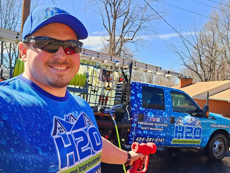 Smiling man in blue shirt and cap posing beside a blue utility truck on a sunny day