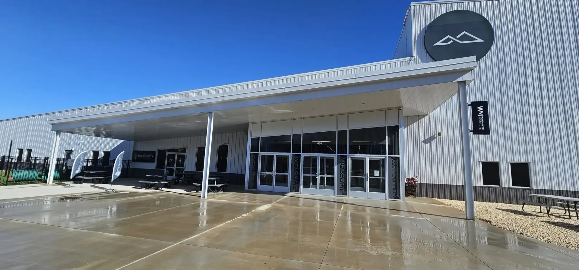 Modern white building with a covered entrance and large glass doors on a wet concrete forecourt