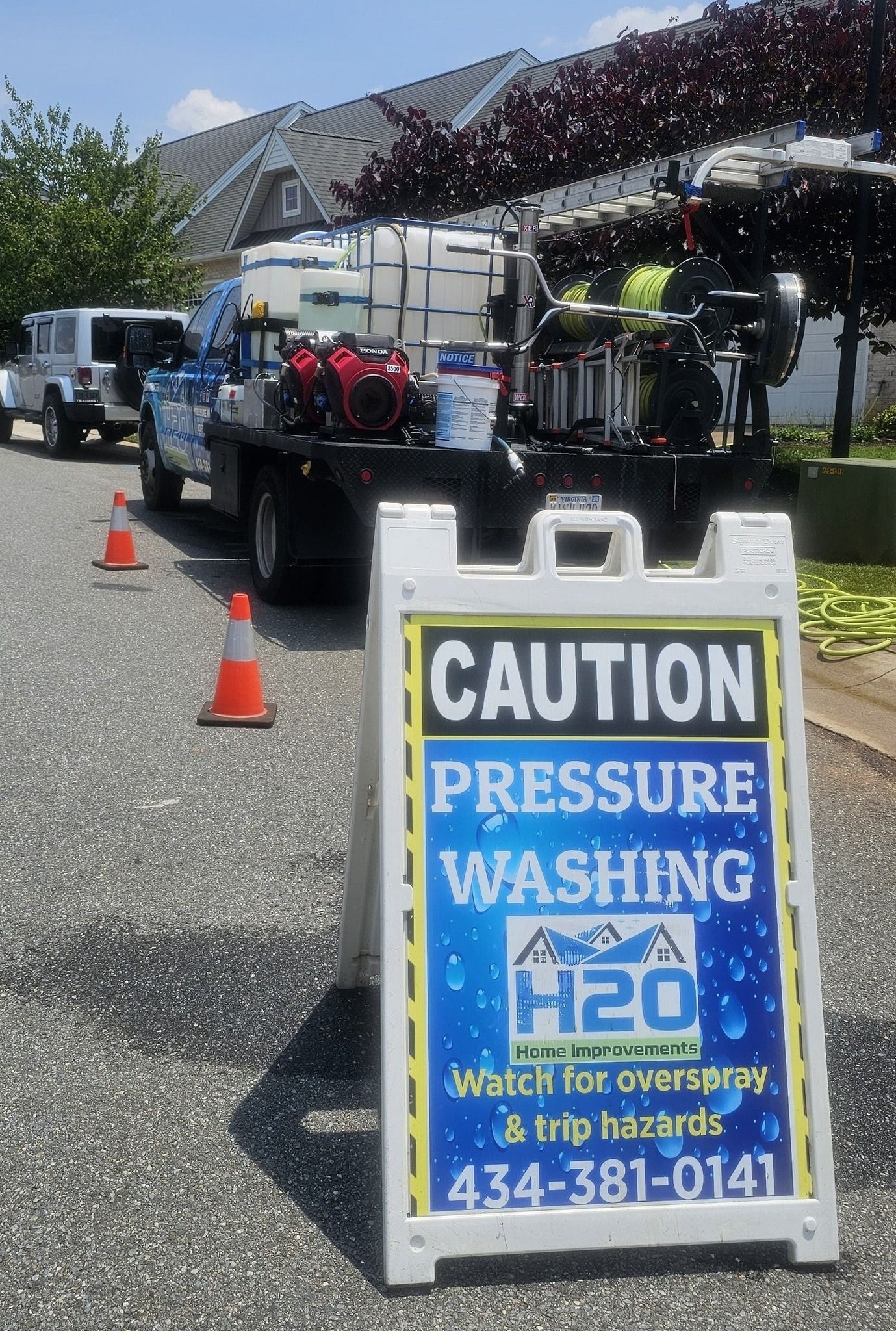 Caution sign for pressure washing in front of a truck and cones on a residential street