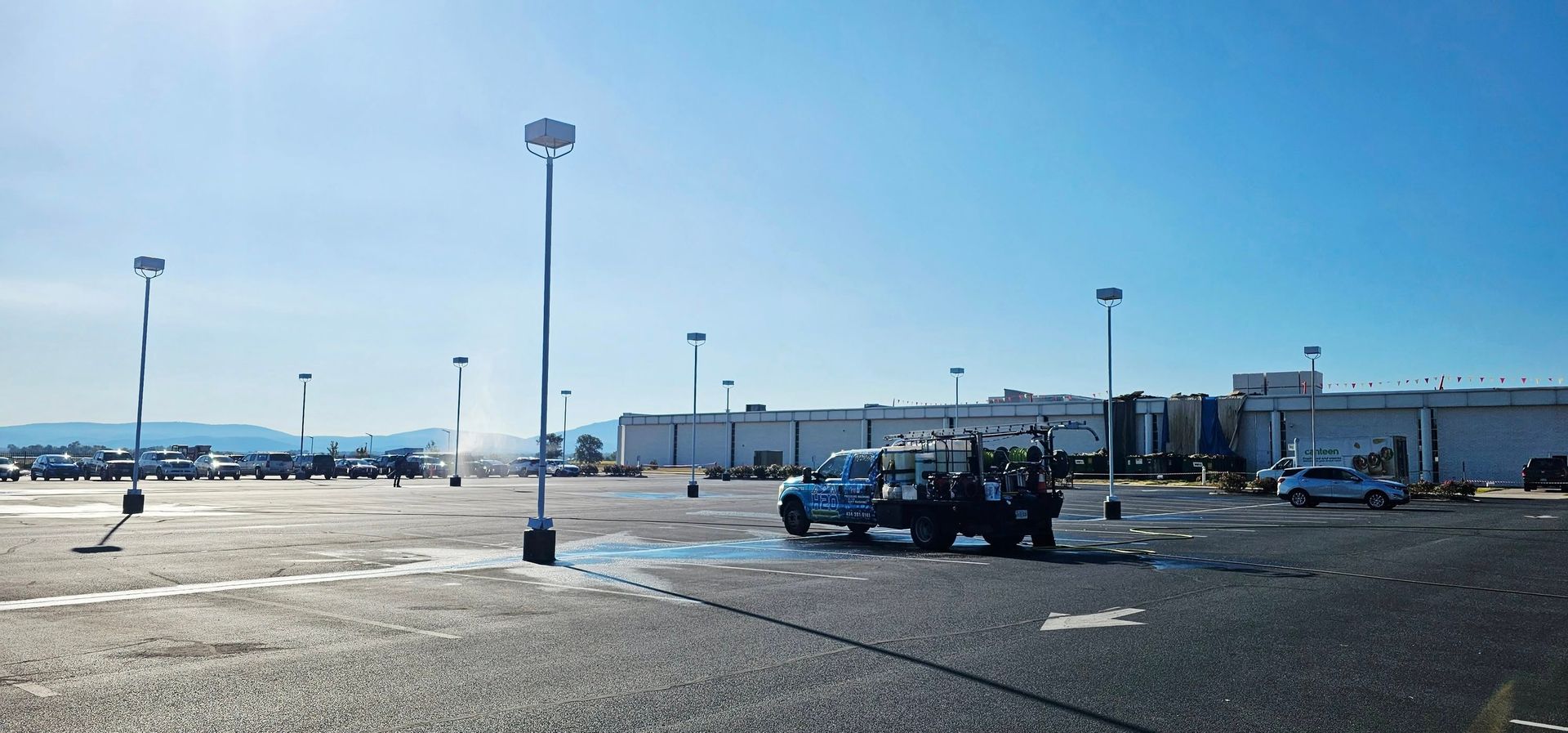 Empty parking lot with a few cars and tall light poles under a clear blue sky