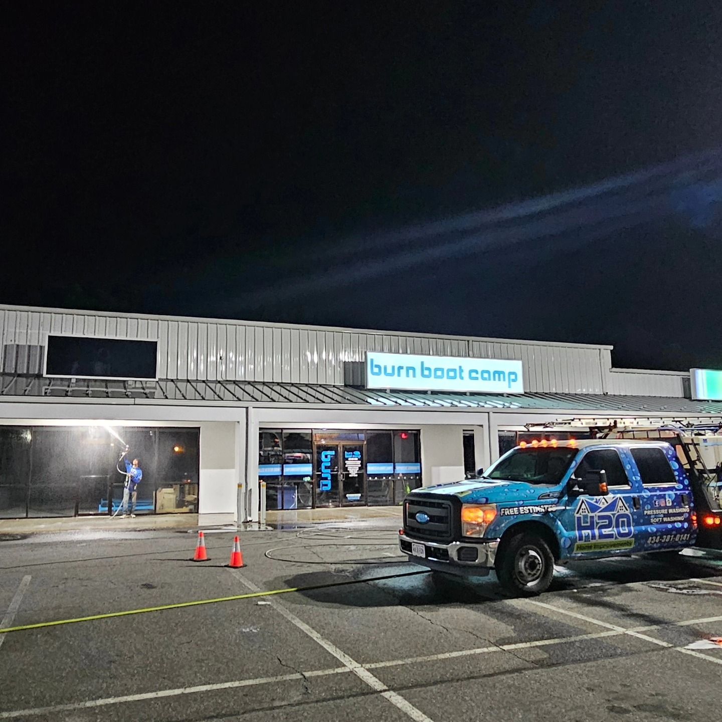 Nighttime at a Burn Boot Camp storefront with a blue emergency vehicle parked outside and cones in the lot
