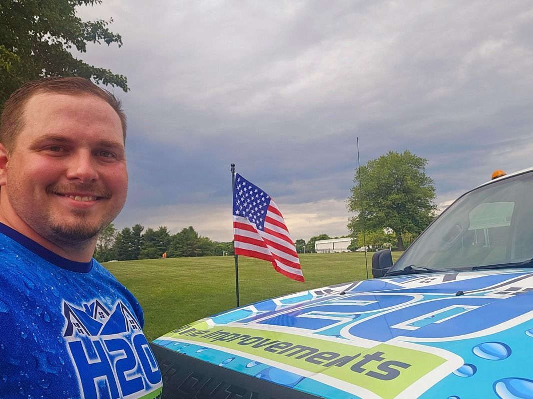 Man smiling beside a blue race car with an American flag at a cloudy outdoor track