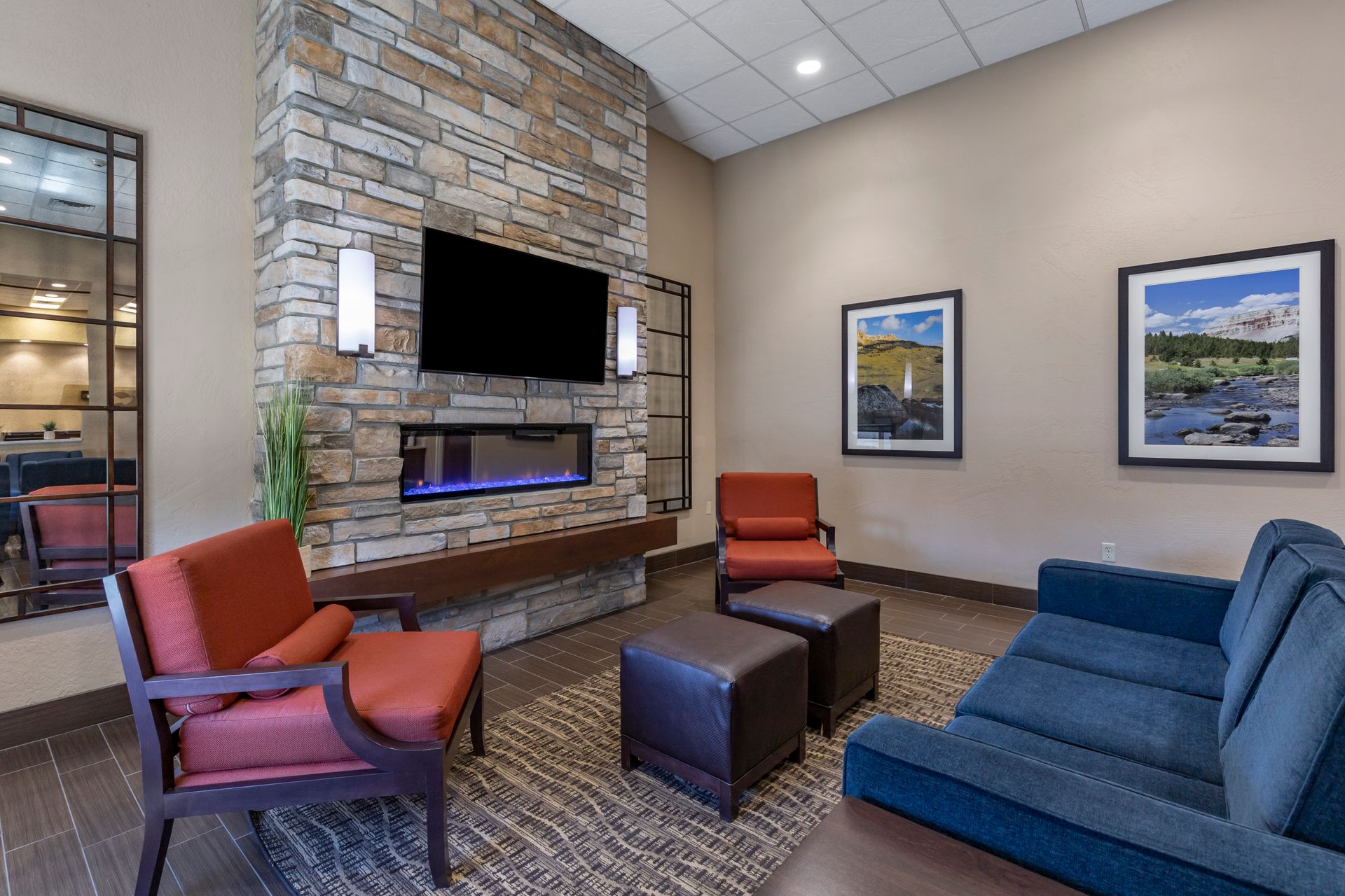 A hotel lobby with a couch , chairs , ottomans and a fireplace.