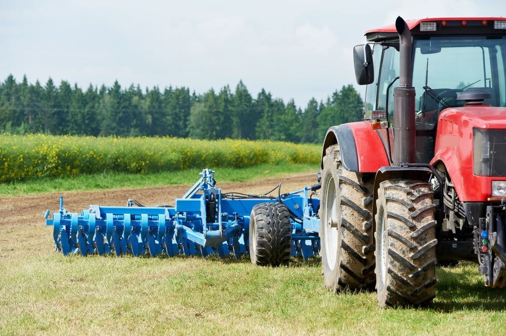 A Red Tractor Is Plowing a Field with A Blue Plow Attached to It — Docs Mobile Tyre Service in Hervey Bay, QLD