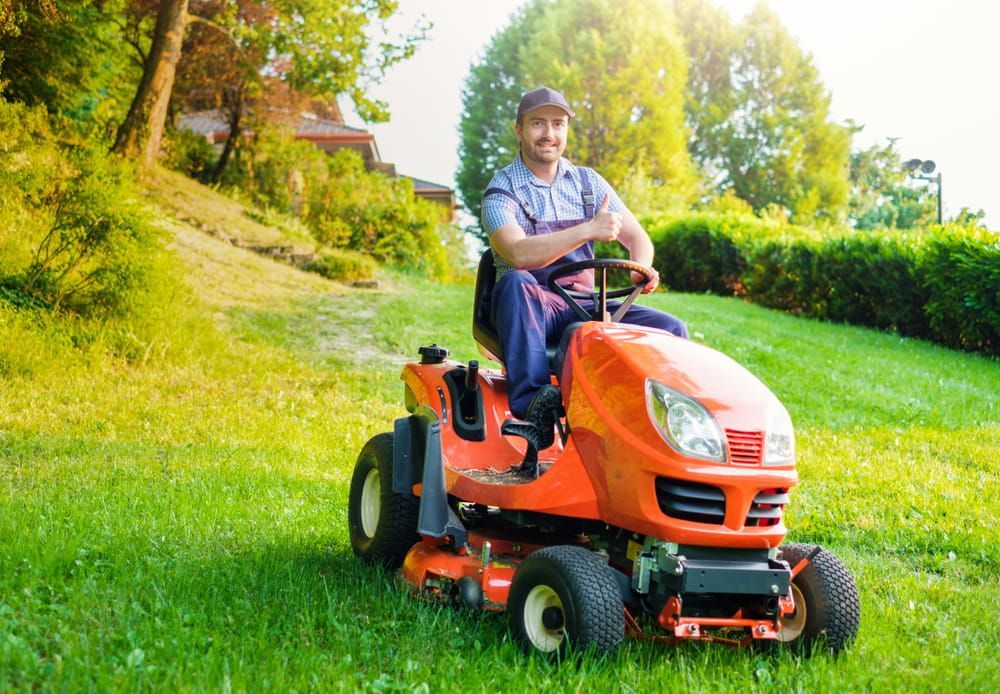 A Man Is Riding a Lawn Mower on A Lush Green Lawn — Docs Mobile Tyre Service in Hervey Bay, QLD