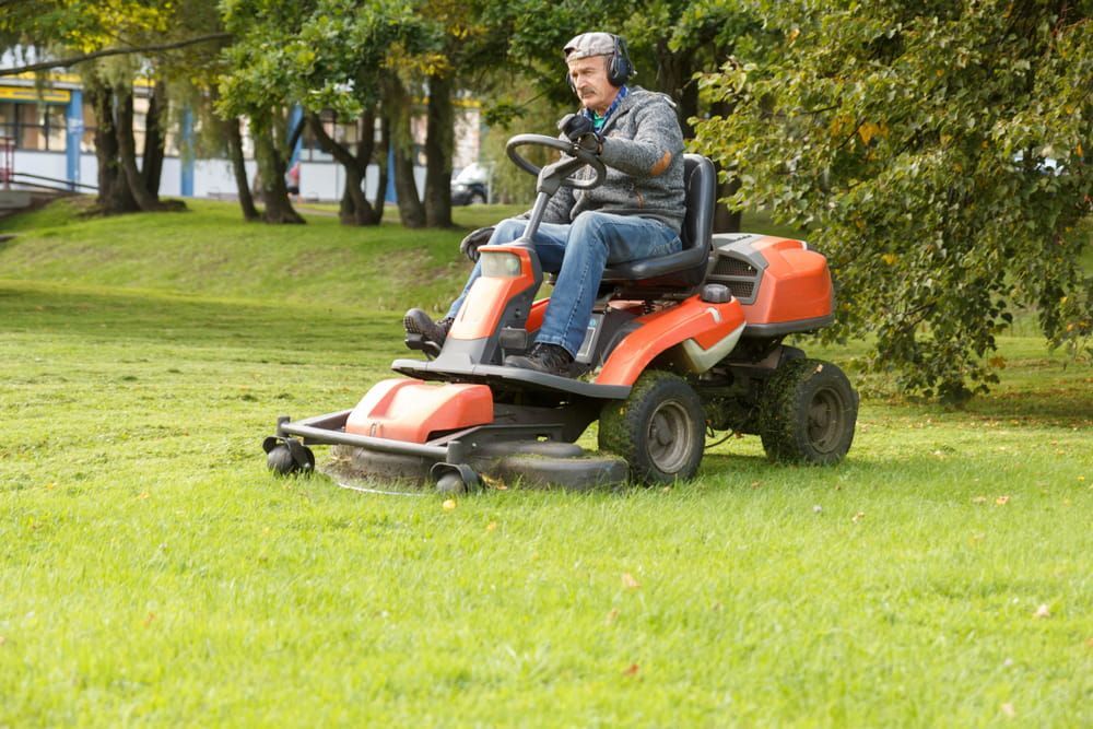 A Man Is Riding a Lawn Mower in A Park — Docs Mobile Tyre Service in Noosa, QLD