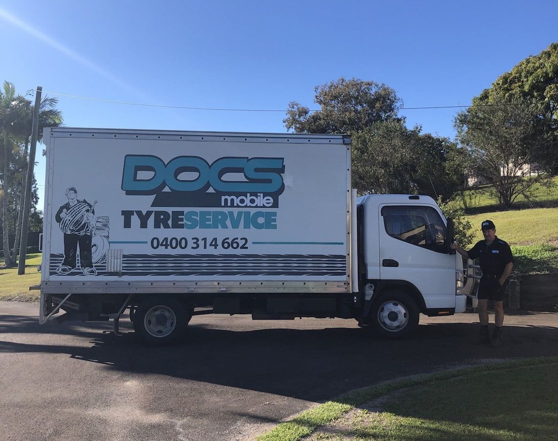 A Man Is Standing in Front of A Docs Mobile Tyre Service Truck — Docs Mobile Tyre Service in Hervey Bay, QLD