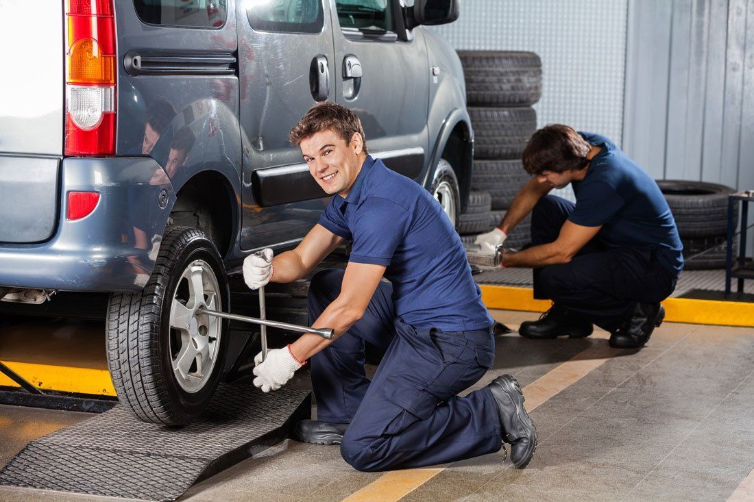 Two Men Are Changing a Tire on A Car in A Garage — Docs Mobile Tyre Service in Hervey Bay, QLD