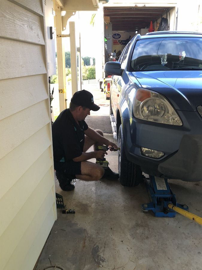 A Man Is Changing a Tire on A Blue Car — Docs Mobile Tyre Service in Noosa, QLD
