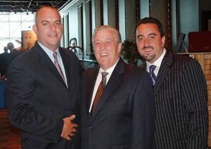 Three men in suits posing together indoors, smiling at the camera.