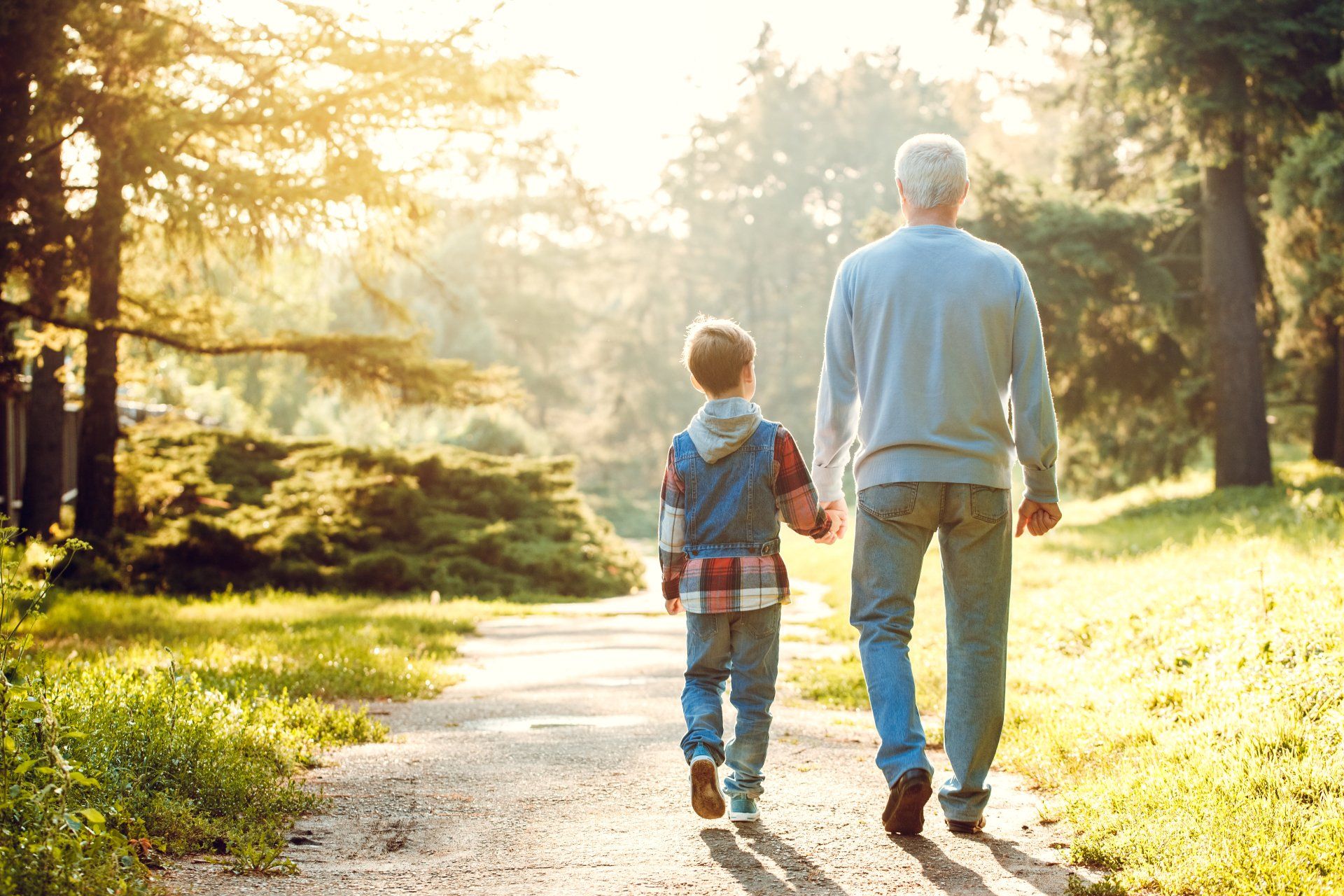 Two people walking hand in hand on a sunlit park path, with trees and warm morning light.