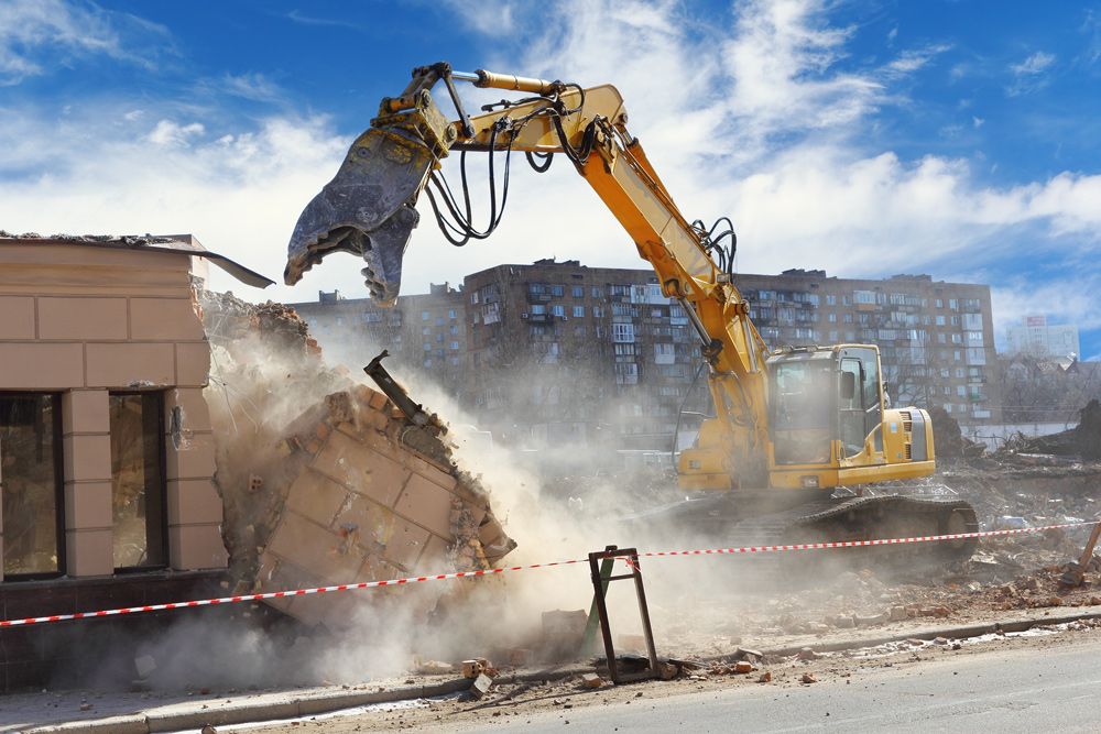 A Yellow Excavator Is Demolishing A Building On A Construction Site — Ballina Demolitions In Ballina, NSW
