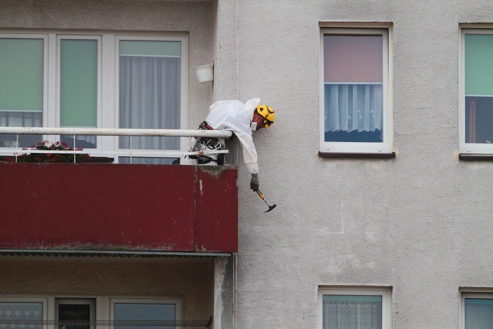 A Man Is Standing On A Balcony Of A Building Holding A Hammer — Ballina Demolitions In Evans Head, NSW
