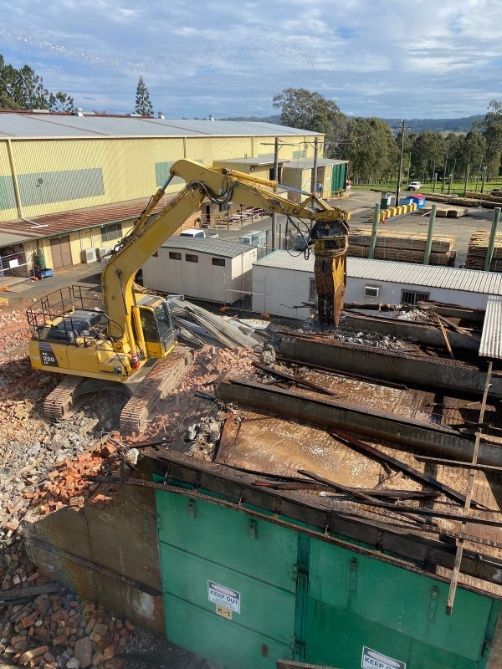 A large excavator using a demolition attachment to break apart a brick and steel structure.