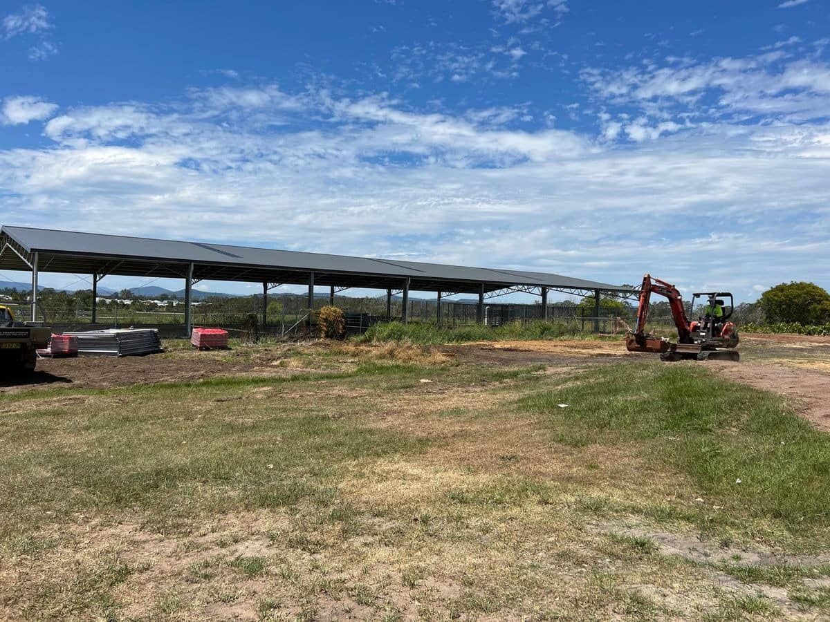 A Red Excavator Is Sitting In A Field Next To A Building — Ballina Demolitions In East Wardell, NSW