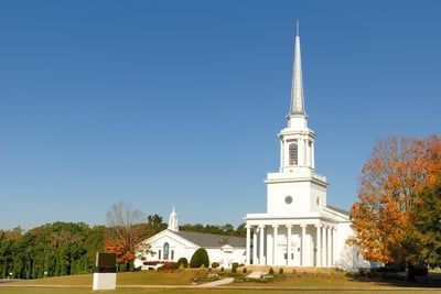A large white church with a steeple in the middle of a field.