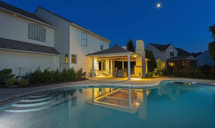 A large swimming pool is in the backyard of a house at night.