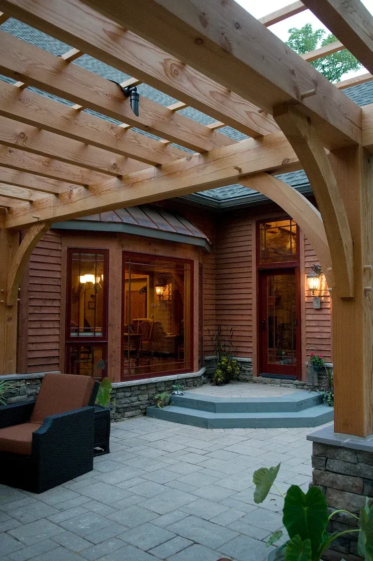 A wooden pergola over a patio in front of a house.