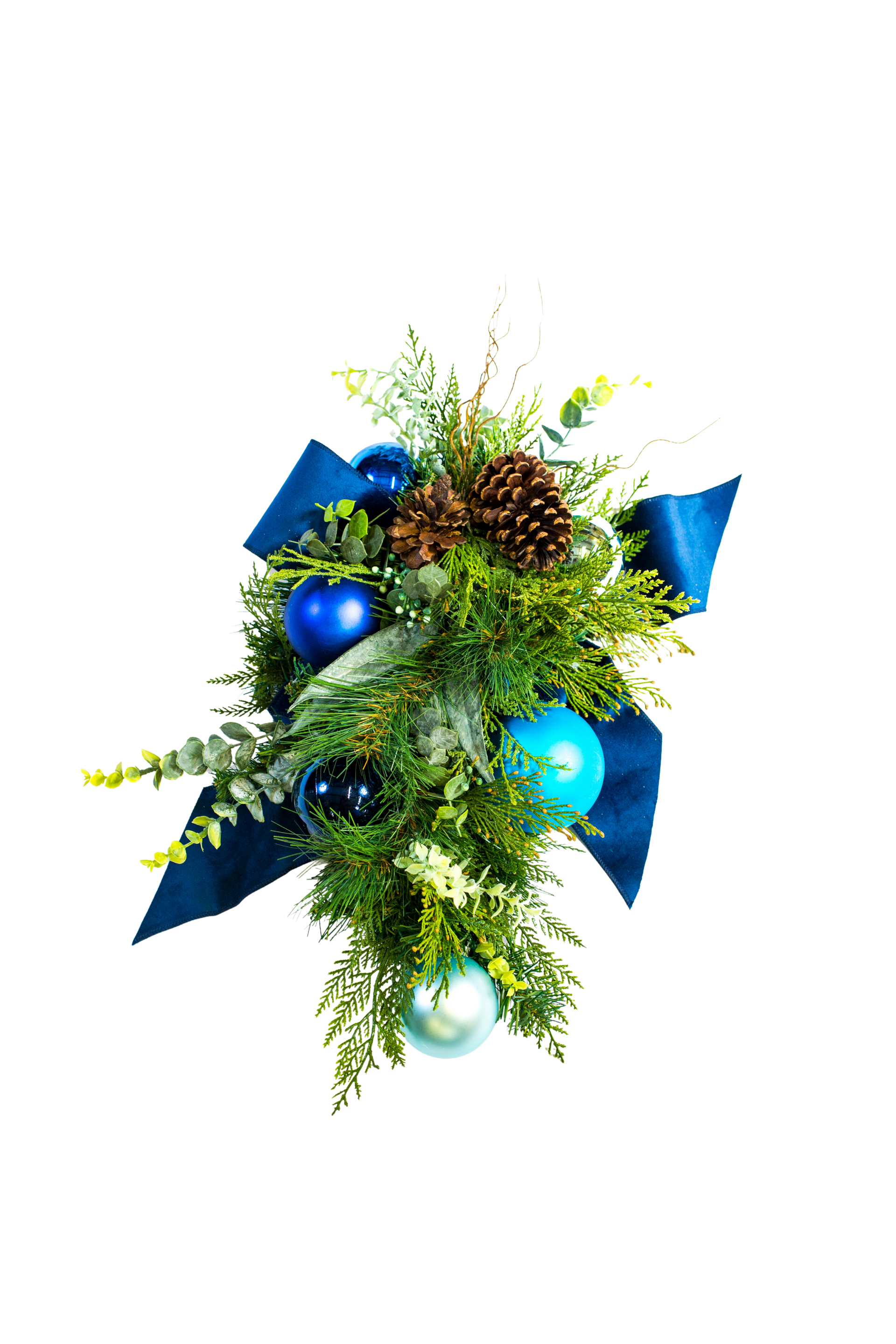 Christmas ornament arrangement with blue baubles, pine cones, greenery, and ribbon against white.