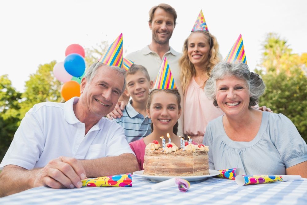A family is sitting at a table with a birthday cake and balloons.