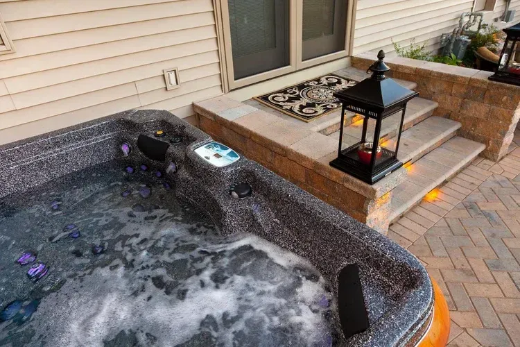 A hot tub is sitting on a brick patio next to a house.