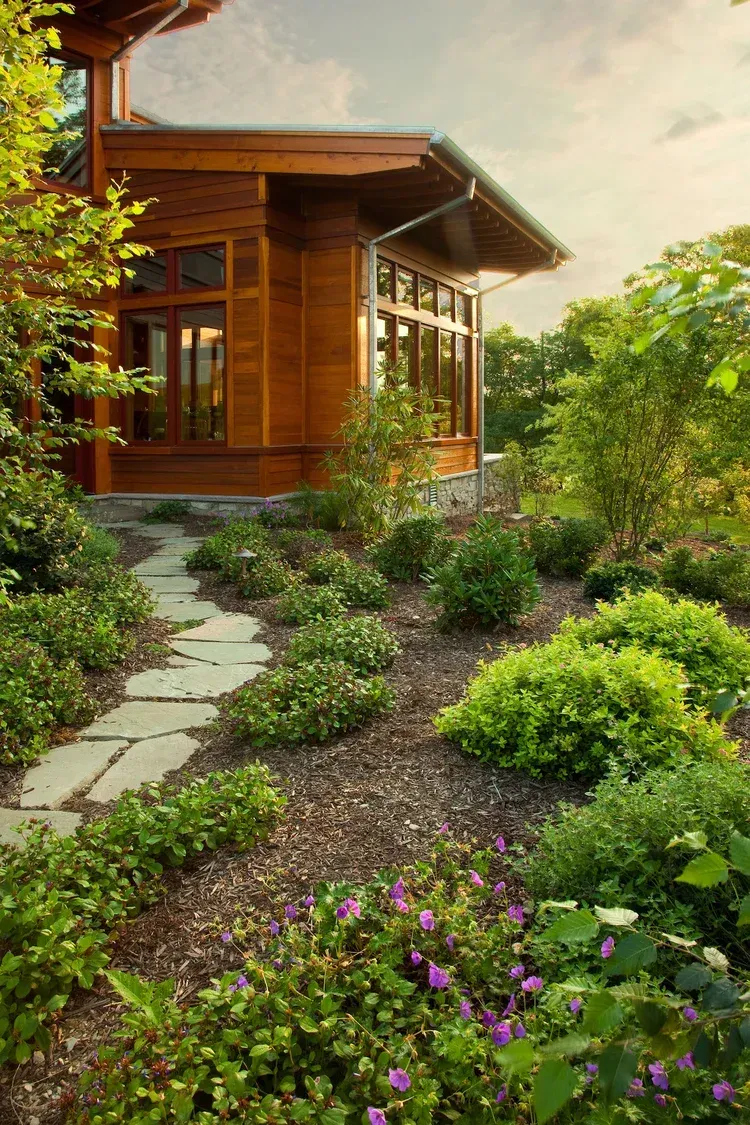 A path leading to a wooden house surrounded by flowers and bushes.