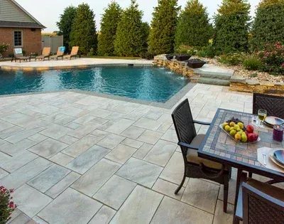 A patio with a table and chairs next to a large swimming pool.