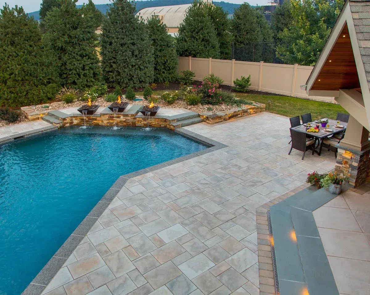 A large swimming pool is surrounded by a patio with a table and chairs.