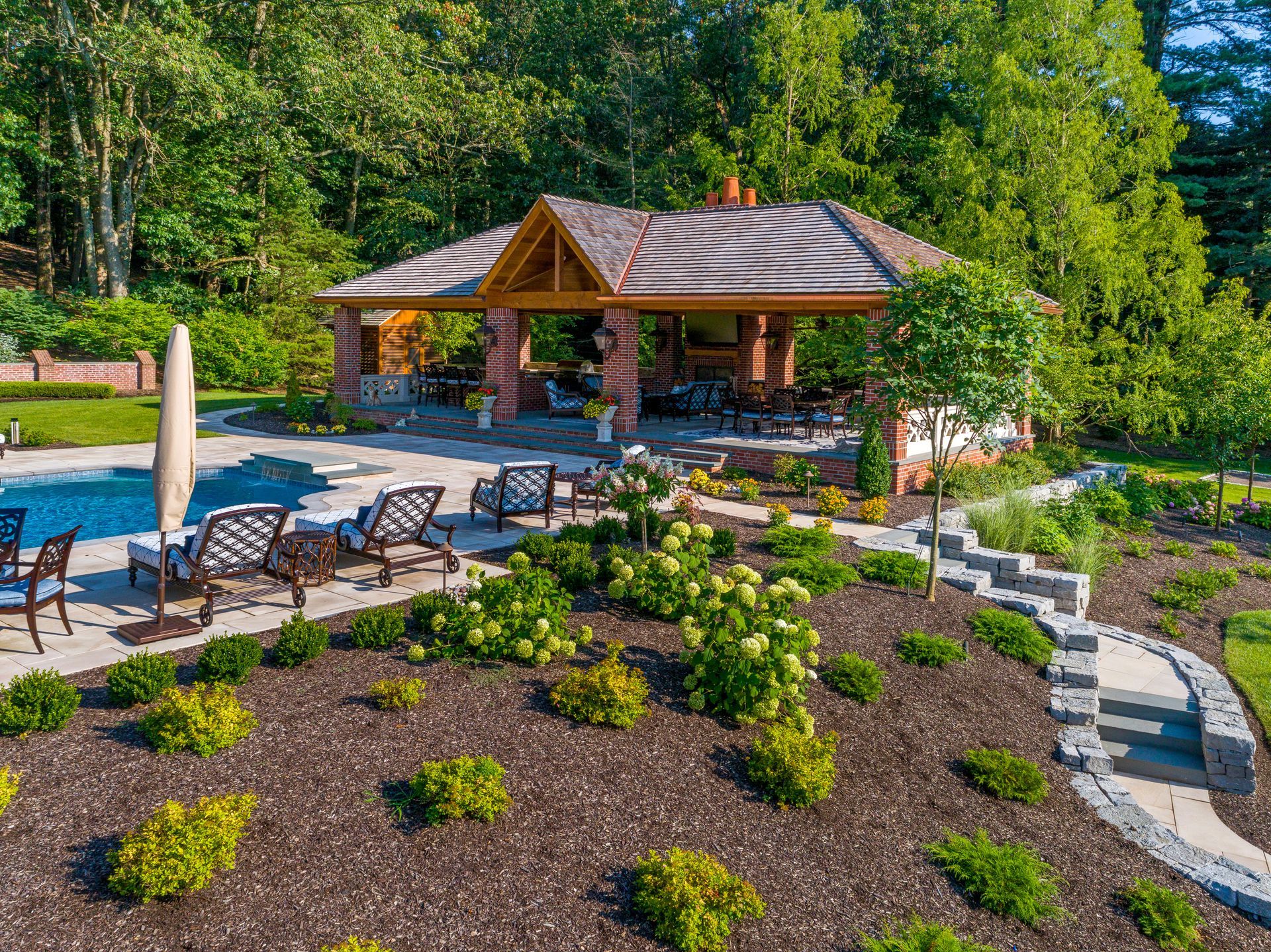 An aerial view of a swimming pool with a gazebo in the backyard surrounded by trees.