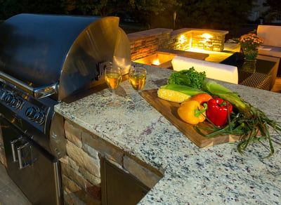 A grill is sitting on top of a granite counter next to a cutting board with vegetables on it.