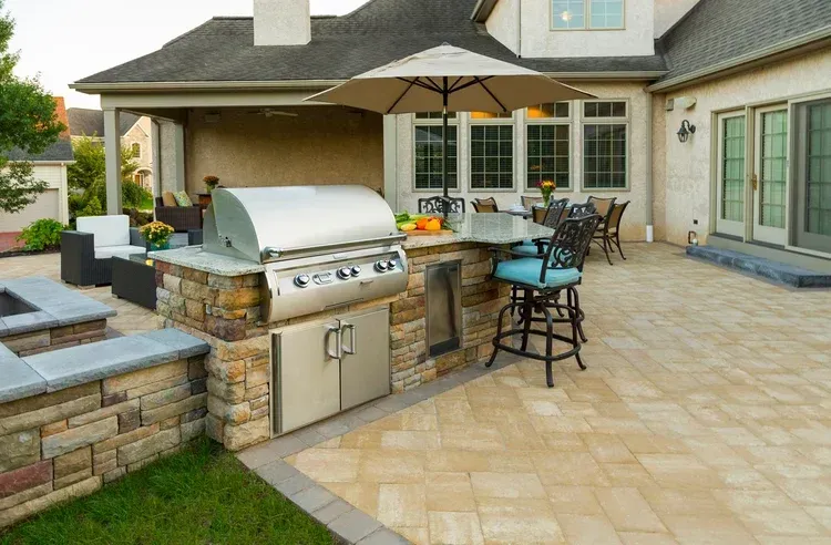 A patio with a grill and umbrella in front of a house.