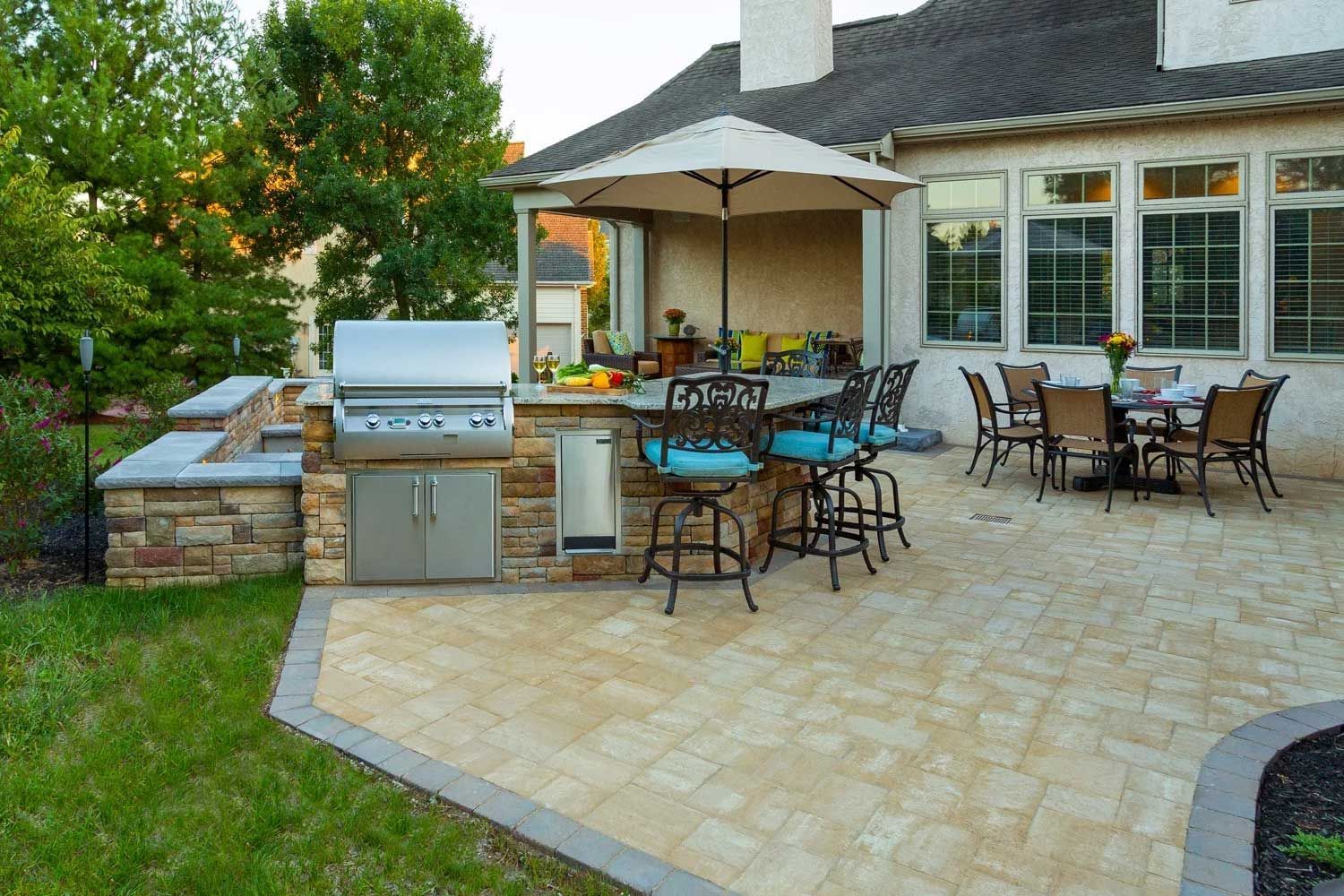 A patio with a grill and tables and chairs in front of a house.