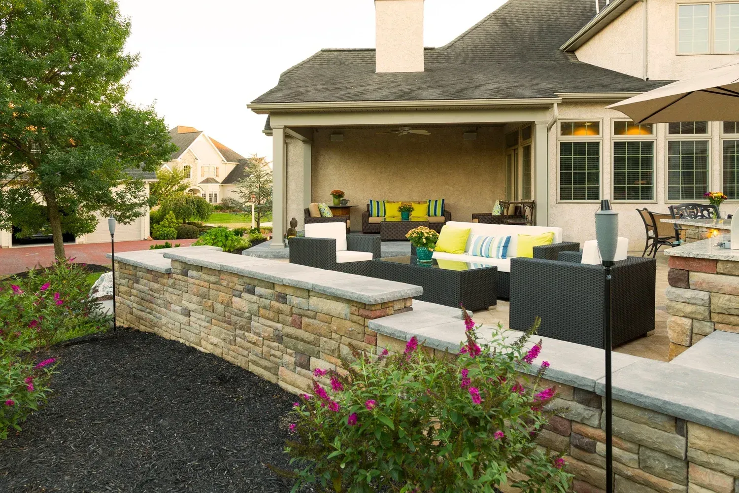 A patio with a stone wall and a couch and chairs in front of a house.