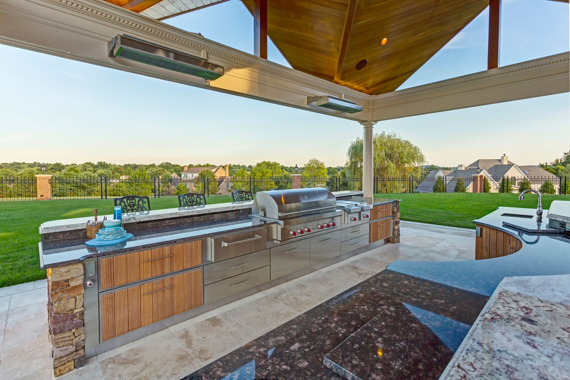 Outdoor kitchen with a grill, countertops, and wooden cabinetry under a covered patio.