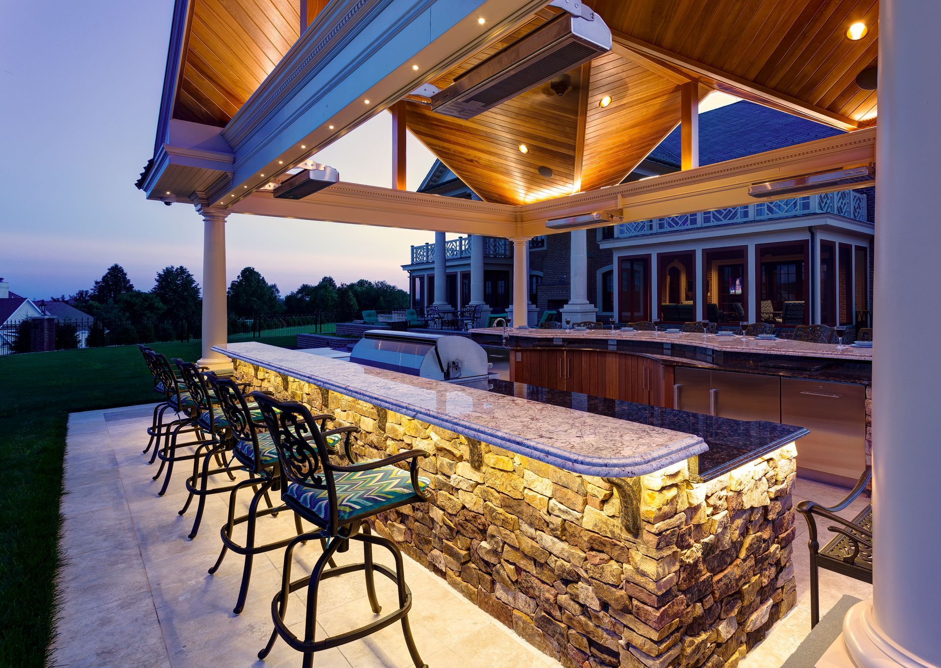 A large outdoor kitchen with a stone counter top and stools