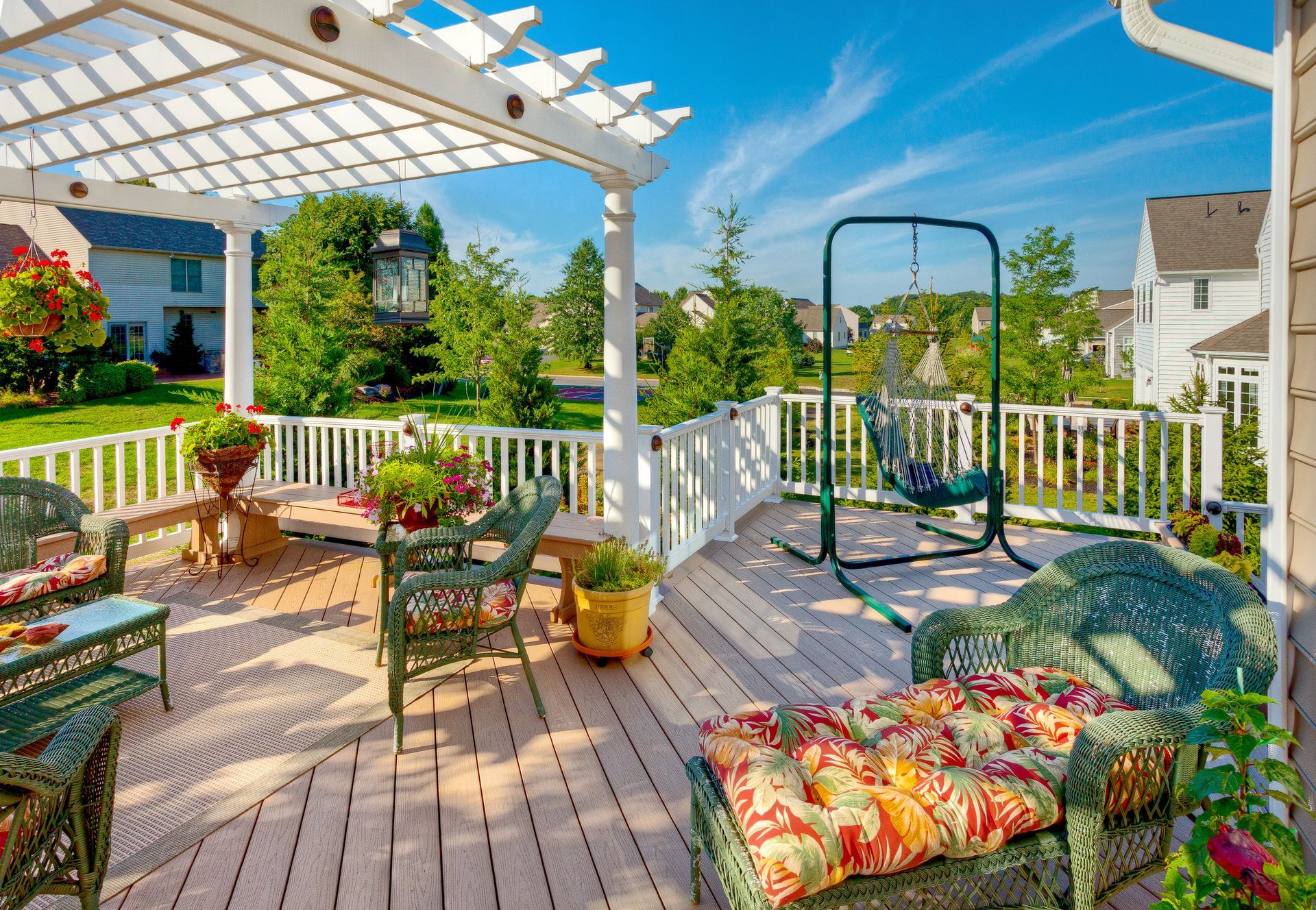 A wooden deck with wicker furniture and a swing under a pergola.