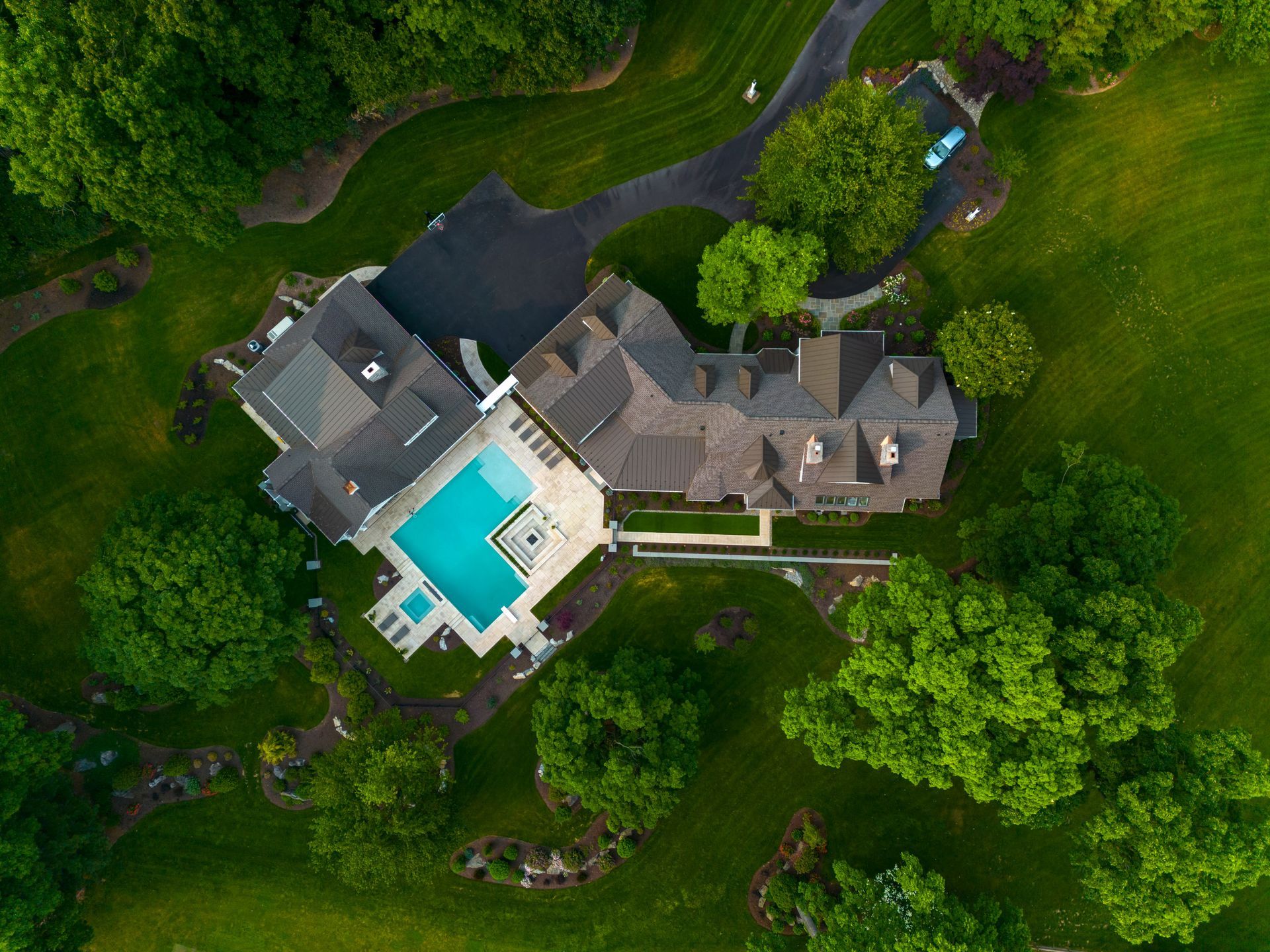 An aerial view of a large house with a swimming pool surrounded by trees.